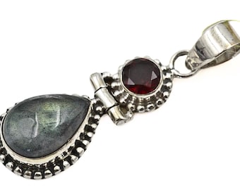 Puede incluir: Colgante de plata con una piedra preciosa gris iridiscente en forma de pera y una piedra preciosa redonda de color rojo intenso. El colgante tiene un engaste de plata decorativo con un lazo para una cadena.