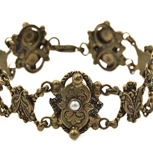 May include: A gold-tone bracelet featuring intricate floral designs and white pearl accents.