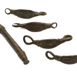 May include: A collection of antique bronze tools, featuring a long-handled tool with a loop and four smaller, leaf-shaped tools with loop handles. The tools have a weathered appearance, suggesting age and use. The background is plain white.