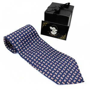 May include: A navy blue tie with a repeating pattern of small red rectangles within white squares. The tie is next to a black gift box with a black ribbon and a business card with a lady illustration.