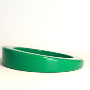 May include: A bright green, glossy, oval-shaped, ceramic trinket dish. The dish is slightly tilted to the side.