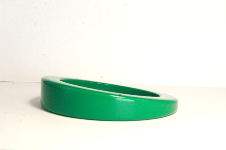 May include: A bright green, glossy, oval-shaped, ceramic trinket dish. The dish is slightly tilted to the side.