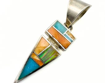 Könnte beinhalten: Silberanhänger mit geometrischem Design. Der Anhänger hat rechteckige und dreieckige Formen mit eingelegten Türkis-, Orange- und schillernden Muschelteilen. Der Anhänger hat oben eine Schlaufe für eine Kette.