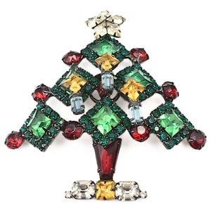 May include: A vintage Christmas tree brooch made of rhinestones in shades of green, red, yellow, and blue. The tree is decorated with a star at the top and a base of clear and yellow rhinestones.