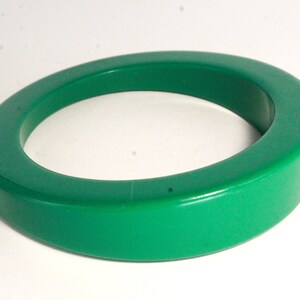 May include: A bright green plastic bangle bracelet. The bracelet is thick and has a rounded shape.