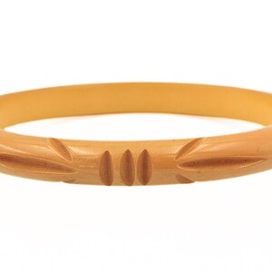 May include: A light brown, round bangle bracelet. The bracelet has carved leaf-like designs. The bracelet is made of a solid material and has a smooth, polished finish. The bracelet is a classic jewelry piece.