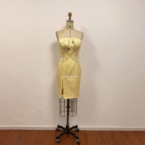 May include: A yellow strapless dress with a floral embroidery design. The dress has a fitted bodice and a straight skirt with a slit on the left side. The dress is displayed on a mannequin.