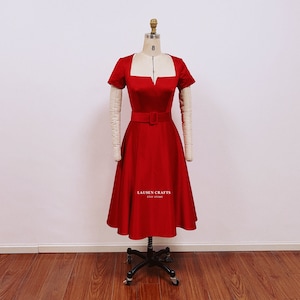 May include: A red satin dress with a square neckline and a fitted bodice. The dress has a full skirt and a belt at the waist. The dress is on a mannequin and the text "LAUSEN CRAFTS ETSY STORE" is printed on the skirt.