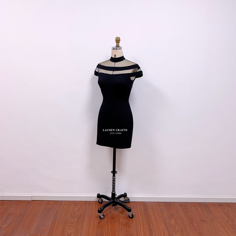 Pu&ograve; includere: Un mini abito nero con collo alto e pannelli in rete trasparente sul d&eacute;collet&eacute; e sulle spalle. L'abito &egrave; esposto su un manichino su sfondo bianco. Il testo "LAUSEN CRAFTS ETSY STORE" &egrave; stampato sull'abito.