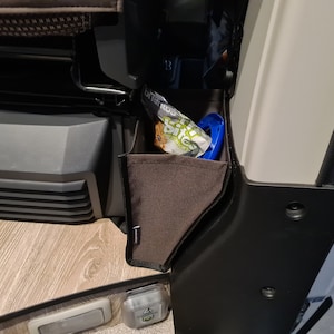 Pode incluir: Um bolso de armazenamento de tecido castanho com guarni&ccedil;&atilde;o preta est&aacute; preso ao lado de um ve&iacute;culo. O bolso est&aacute; cheio de um saco de guloseimas para c&atilde;es e um brinquedo de pl&aacute;stico azul.