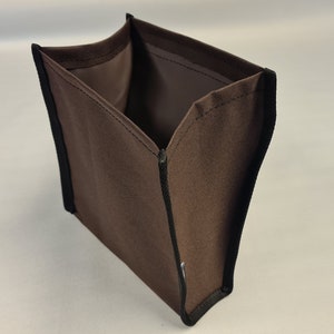 Pode incluir: Um cubo de armazenamento de tecido castanho com guarni&ccedil;&atilde;o preta. O cubo est&aacute; vazio e aberto, mostrando o interior.