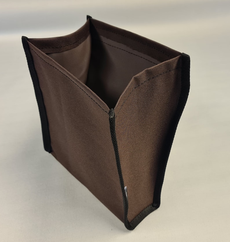 Pode incluir: Um cubo de armazenamento de tecido castanho com guarni&ccedil;&atilde;o preta. O cubo est&aacute; vazio e aberto, mostrando o interior.