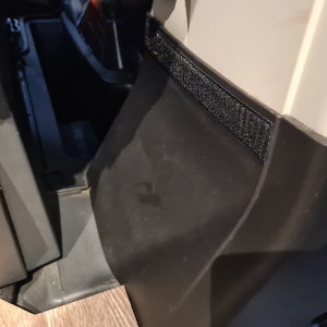 Pode incluir: Close-up de um painel de pl&aacute;stico preto com uma tira de velcro preto.