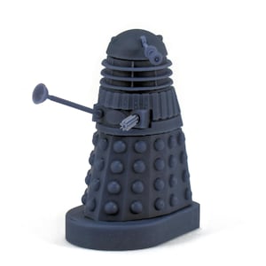 May include: A blue plastic toy robot with a dome-shaped head and a single eye. The robot has a long, thin arm with a round end. The robot is standing on a base.