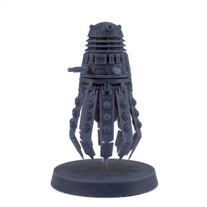 May include: A gray, detailed model of a Dalek, a fictional alien race from the British science fiction television series Doctor Who. The Dalek is standing on a round base.