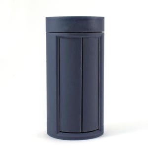 May include: A dark blue cylindrical container with a smooth, matte finish. The container has a lid and a vertical seam down the centre.