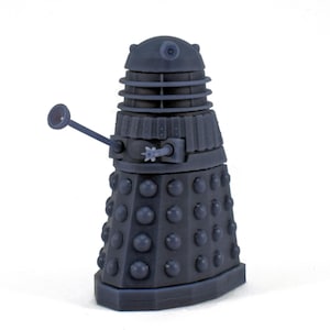 Könnte beinhalten: Dunkelgraue Dalek-Figur, eine fiktive außerirdische Rasse aus der britischen Science-Fiction-Fernsehserie Doctor Who. Die Figur hat einen zylindrischen Körper mit zahlreichen runden Vorsprüngen, einen schrägen Mittelteil und einen kuppelförmigen Kopf.
