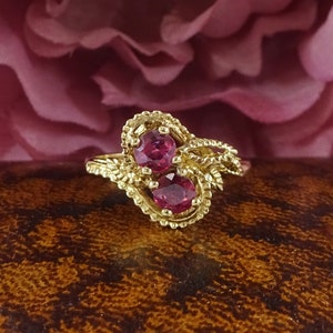 May include: A gold ring featuring two ruby red stones set in a delicate, leafy design.