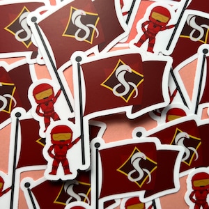 May include: A collection of red and white stickers featuring a stylized snake design and a cartoon character wearing a helmet. The stickers are arranged in a random pattern on a pink surface.