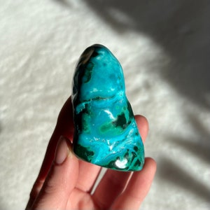 May include: A smooth, polished green and blue gemstone with swirling patterns. The gemstone is a natural crystal and has a unique, organic shape.