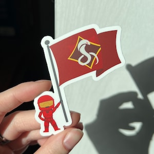 May include: A red and white sticker featuring a cartoon character holding a red flag with a white snake logo and the text "S" inside a diamond shape.