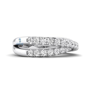 Puede incluir: Un anillo plateado con dos bandas, cada una incrustada con peque&ntilde;as piedras preciosas transparentes. Las bandas se entrelazan, creando un dise&ntilde;o &uacute;nico y elegante. El anillo se muestra sobre un fondo blanco, resaltando su brillo y detalle. La palabra "shanti" es visible.