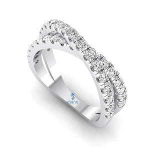 Puede incluir: Un anillo cruzado de oro blanco con dos bandas, cada una incrustada con peque&ntilde;as piedras preciosas redondas y transparentes. El anillo tiene una superficie pulida y reflectante y un dise&ntilde;o moderno. El anillo est&aacute; sobre un fondo blanco.