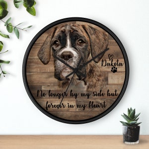 Może przedstawiać: Czarny zegar w ramie z drewnianym tłem, na kt&oacute;rym widnieje brązowy i biały pies rasy boxer. Zegar ma czarne wskaz&oacute;wki i napis "No longer by my side but forever in my heart" oraz "Dakota" z sercem i odciskiem łapy.