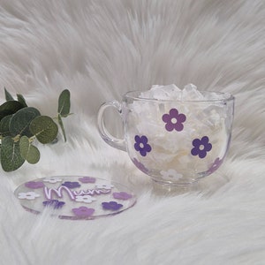 May include: A clear glass mug with a purple flower design and the word "Mum" on a matching coaster. The mug is filled with white tissue paper.