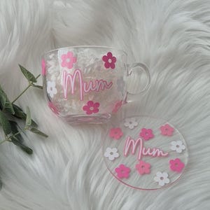 May include: A clear glass mug with a pink and white floral design and the word "Mum" in pink lettering. The mug comes with a matching coaster.