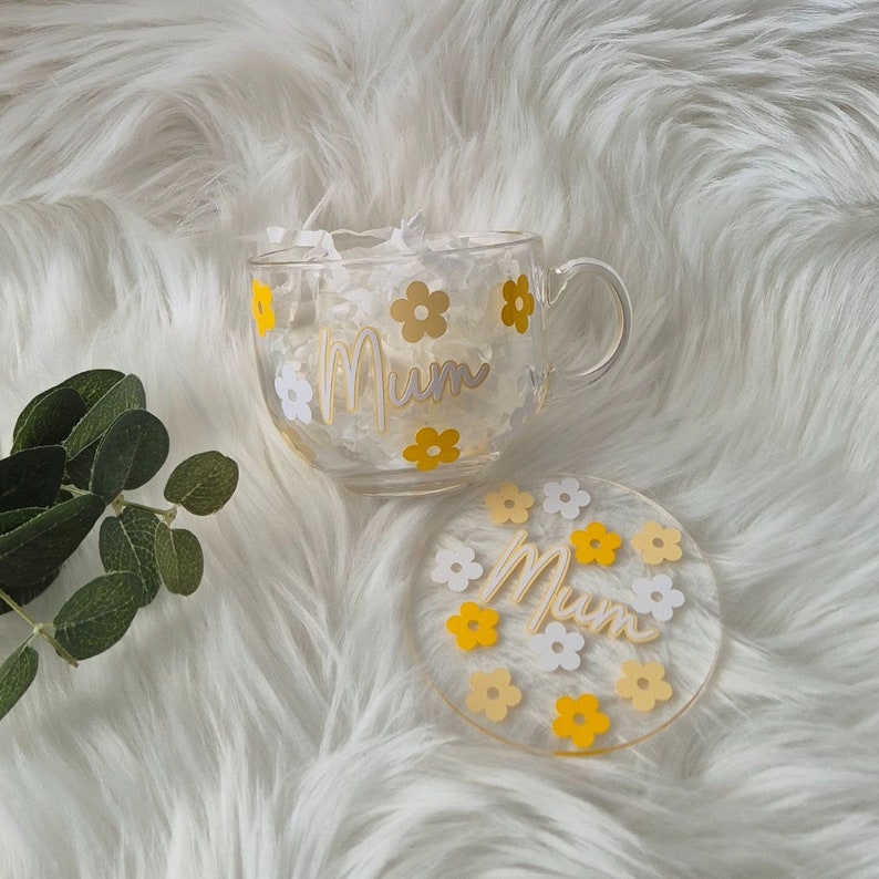 May include: A clear glass mug with a yellow and white floral design and the word "Mum" in gold lettering. The mug comes with a matching coaster.