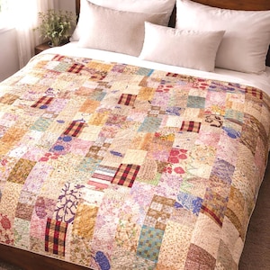 May include: A patchwork quilt featuring a variety of rectangular fabric pieces in diverse patterns, including floral prints, red and black buffalo checks, and textured weaves in shades of yellow, pink, blue, and brown, covering a bed with white pillows.