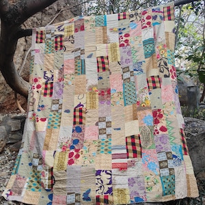 Könnte beinhalten: Eine Patchwork-Decke mit einer Vielzahl von Stoffmustern und -farben, darunter Blumen-, Karo- und geometrische Designs. Die Decke besteht aus rechteckigen und quadratischen Stoffstücken, die zusammengenäht sind und eine strukturierte Oberfläche bilden. Die Farbpalette umfasst Beige, Rot, Blau und Lila.