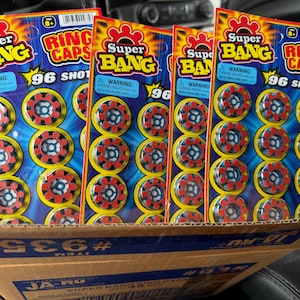 May include: Four packages of Super Bang Ring Caps, each containing 96 shots. The packaging features a blue and yellow design with red and black ring caps visible. The packages are in a cardboard box.