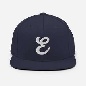 Könnte beinhalten: Eine marineblaue Baseballkappe mit einem weißen, gestickten, kursiv geschriebenen Buchstaben "E" auf der Vorderseite.