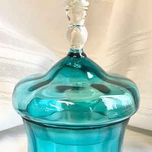 Puede incluir: Un tarro de vidrio de color turquesa con tapa y pomo de vidrio transparente. El tarro tiene una base bulbosa y una parte superior acampanada, con un diseño ondulado. La tapa tiene forma de hongo. El tarro mide aproximadamente 20 cm de alto.