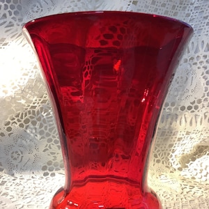 May include: A deep red glass vase with a flared top and a rounded base. The vase has a smooth, glossy finish.