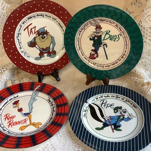 以下が含まれることがあります： ルーニー・テューンズのキャラクターが描かれたセラミック製のディナー皿4枚セット。各皿は、赤、緑、青、または白黒の格子模様の縁取りが施され、白い中心部分には、タズ、バックス・バニー、ロード・ランナー、ペペ・ル・ピューの異なるキャラクターが描かれています。各皿には、キャラクターのセリフが書かれています。