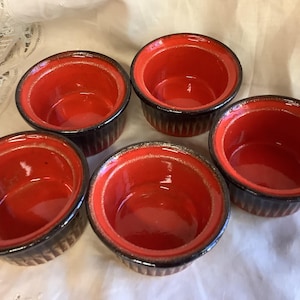Op de afbeelding: Vijf rode en zwarte keramische ramekins. De ramekins zijn rond en hebben een zwarte rand. Ze zijn allemaal even groot en hebben dezelfde vorm.