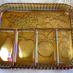 May include: An iridescent amber glass serving tray with four compartments. The tray has embossed fruit designs, including grapes, apples, pears, and plums. The rim has a beaded edge and rounded handles.