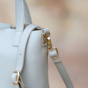 the details of the light beige leather bag, such as the stitching, the buckle, etc., are shown more closely, where you can appreciate its craftsmanship.