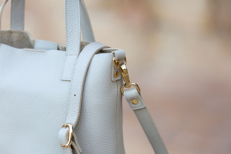 the details of the light beige leather bag, such as the stitching, the buckle, etc., are shown more closely, where you can appreciate its craftsmanship.