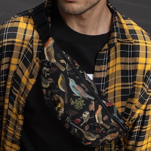 May include: A black fanny pack with a zipper closure and a colorful bird print design. The fanny pack is worn by a person wearing a yellow and black plaid shirt.