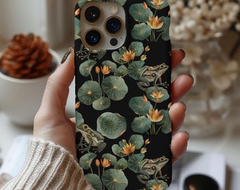 May include: A black phone case with a floral and frog design. The case has a green, brown, and gold color scheme. The case has a camera lens cutout and a cutout for the phone's buttons.