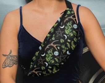 May include: A black fanny pack with a green, black, and white print featuring moons, antlers, and pentagrams. The fanny pack is worn by a person with a tattoo of a moth on their arm.