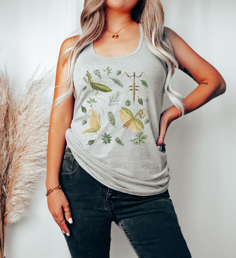 Op de afbeelding: Een grijs tanktop met een print van groene en bruine wandelende takken en bladeren.