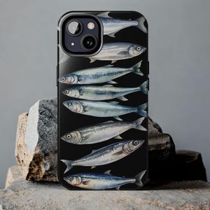 以下が含まれることがあります： 黒い電話ケースに、黒い背景に複数の銀色の魚がデザインされています。電話ケースにはカメラレンズの切り抜きがあります。
