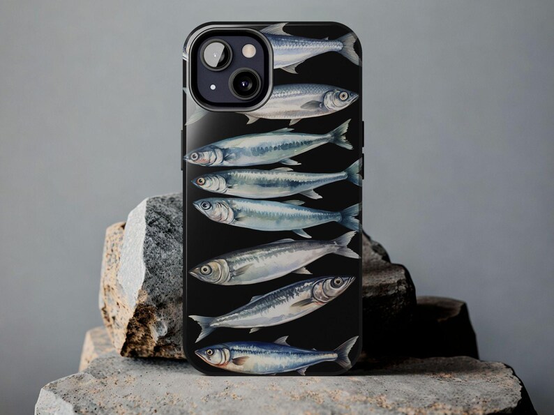 以下が含まれることがあります： 黒い電話ケースに、黒い背景に複数の銀色の魚がデザインされています。電話ケースにはカメラレンズの切り抜きがあります。