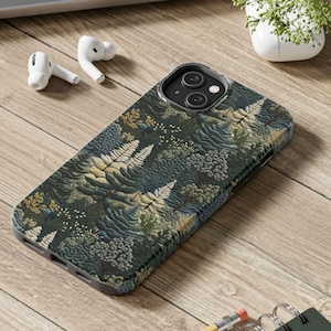 May include: A phone case with a dark green, blue, and white floral pattern. The case is designed for an iPhone with a camera bump.