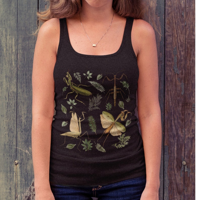 Op de afbeelding: Een zwart tanktop met een print van groene en bruine wandelende takken en bladeren op een zwarte achtergrond.